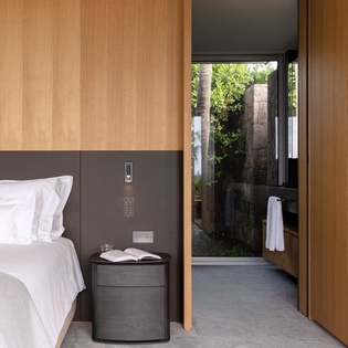 Unwind in your modern bedroom with warm wood accents and a private outdoor bathroom featuring lush garden views.