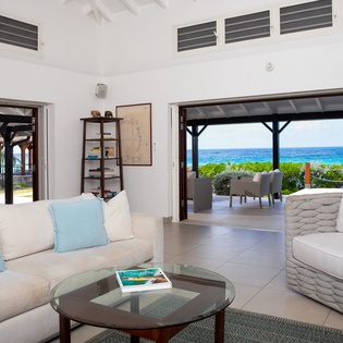 Your bright, airy living space frames breathtaking ocean views through dramatic open doorways. Sink into plush seating with coastal breezes flowing in, steps from the turquoise water.