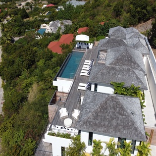 Aerial view captures a modern luxury villa with a pool, sun deck, and tropical garden setting in a quiet residential neighborhood.