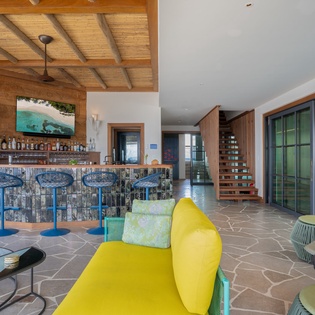 Step into your vibrant social hub with exposed beams, colorful seating, and a stunning bar perfect for evening cocktails.