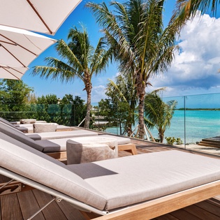 Stretch out on luxurious sunbeds under swaying palms, where crystal-clear turquoise waters create your perfect tropical backdrop for ultimate relaxation.