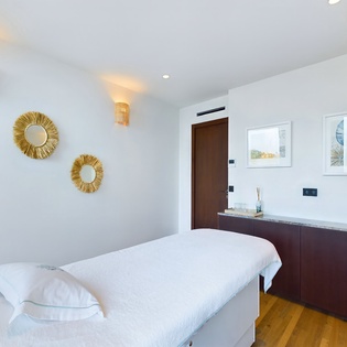 Unwind in this serene spa treatment room where tranquil white linens and warm golden accents create your perfect wellness sanctuary.