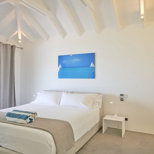 Your peaceful retreat features a plush king bed beneath exposed white beams, with ocean-inspired art setting a serene mood.