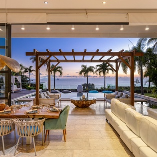 Step into your elegant open-plan living space where modern luxury meets tropical paradise through floor-to-ceiling windows.