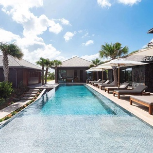 Your private tropical oasis awaits with a sparkling pool, cushioned loungers under umbrellas, and swaying palms framing modern pavilions under sunny Caribbean skies.