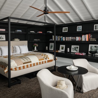 Unwind in your sophisticated retreat with floor-to-ceiling built-in bookshelves, a striking four-poster bed, and cozy seating area perfect for quiet evenings.