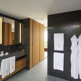 Step into your luxurious spa-like bathroom with sleek black marble walls, warm wood accents, and plush white towels awaiting your arrival.