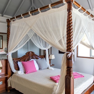 Drift into tropical dreams beneath flowing mosquito netting in your elegant four-poster bed sanctuary.