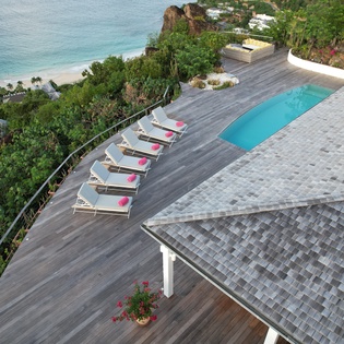 Aerial view of luxury villa with pool terrace overlooking pristine beach and turquoise waters.