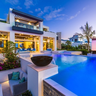 Modern luxury villa features an expansive pool and multiple terraces at twilight, surrounded by lush tropical landscaping and contemporary outdoor living spaces.