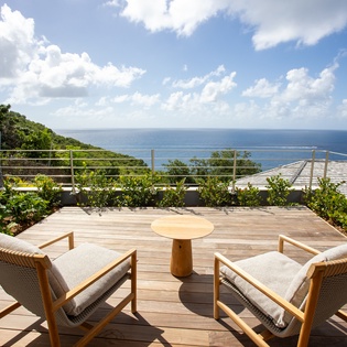 Picture yourself unwinding in this stunning oceanfront terrace, where comfortable seating meets breathtaking sea views through tropical greenery.