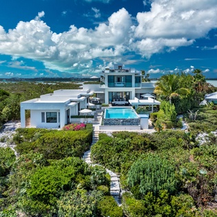 Stunning modern waterfront villa surrounded by lush tropical gardens and natural landscape, featuring multiple levels with a private pool and expansive outdoor terraces overlooking the pristine coastal scenery.