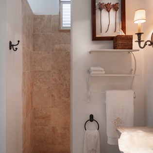 Step into your spa-like bathroom featuring natural stone tiles, warm sconce lighting, and plush towels ready for your use.