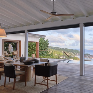 Panoramic coastal vistas frame your dining experience, where a stylish setting opens onto the sparkling sea and hillside village beyond.