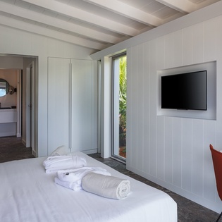 Unwind in your bright, modern bedroom with crisp linens, exposed beams, and a wall-mounted TV for cozy evenings.