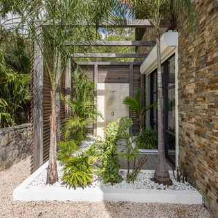 Modern tropical entrance with natural stone walls and lush landscaping creates a serene arrival experience.