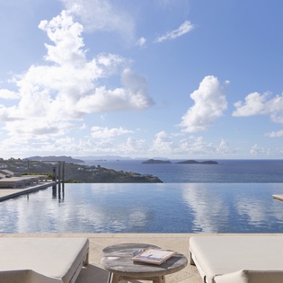 An infinity pool overlooking the shimmering Aegean and distant islands creates a serene oasis for your escape.
