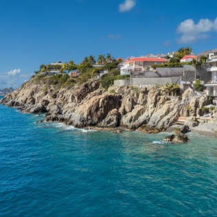 Stunning clifftop villas perched above crystal-clear Caribbean waters with dramatic rocky coastline and colorful rooftops creating a picturesque tropical setting.