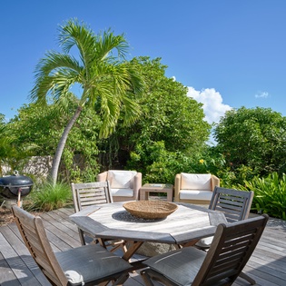 Relax on your private deck surrounded by tropical palms, where outdoor dining meets paradise under endless blue skies.