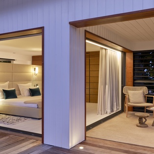 Step into your serene retreat where the bedroom opens to a private covered terrace, inviting you to unwind in comfortable seating while soft lighting creates a warm, intimate atmosphere.