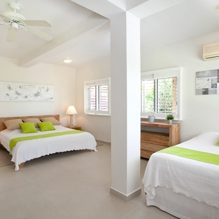 Your light-filled sleeping quarters feature crisp linens with vibrant green accents, ceiling fans, and climate control to keep you comfortable in tropical warmth. Thoughtful touches like bedside lamps and natural wood furnishings create a serene retreat af