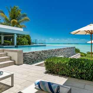 Beachfront infinity pool and terrace area with modern design, tropical landscaping, and direct ocean access on a sunny day.