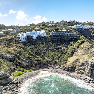 Stunning clifftop homes overlook a secluded cove with turquoise waters and dramatic rocky coastline below.