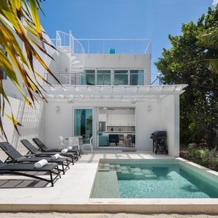 Modern two-story villa featuring a private pool, sun loungers, and tropical landscaping in a pristine outdoor setting.