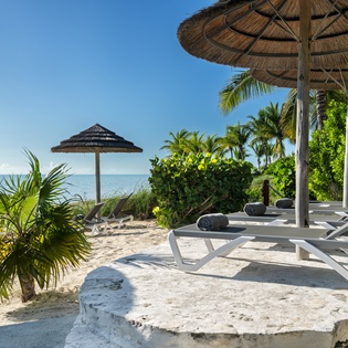 Your private beachfront paradise with loungers under thatched umbrellas, where soft sand meets crystal-clear waters for ultimate relaxation.