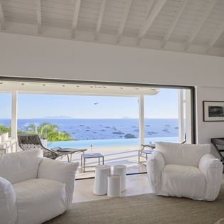 Sink into plush white furniture while soaking in breathtaking ocean vistas through floor-to-ceiling windows in your serene living space.