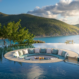 Spectacular infinity pool with sunken seating area overlooking pristine turquoise waters and lush mountains.