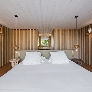 Drift off in your serene wooden sanctuary with crisp white linens and warm pendant lighting creating the perfect atmosphere for rest.