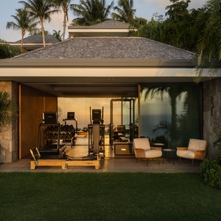 Your private fitness pavilion awaits with professional equipment and comfortable seating, all framed by tropical palms and warm evening light.