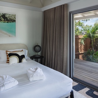 Your peaceful bedroom opens to a private deck surrounded by lush tropical gardens, where crisp linens and modern comfort await your arrival.