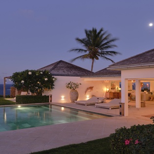 A stunning tropical retreat bathed in twilight, where a pristine pool reflects the moonlight and an elegant covered patio invites endless evenings by the sea.
