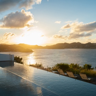 Stunning infinity pool overlooks mountains and ocean at golden hour, creating a breathtaking tropical paradise setting.
