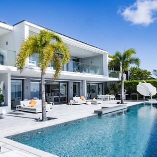 Sleek modern villa featuring pristine swimming pool, tropical landscaping, and contemporary architecture under clear blue skies.