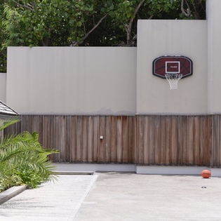 The property features a private basketball court area with a regulation hoop, set against modern architectural walls and surrounded by lush tropical greenery.