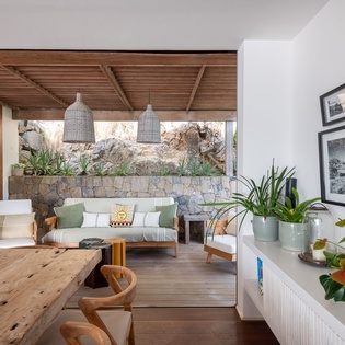 Sink into the inviting sofa under rustic wood beams, where natural light streams in and lush plants frame every corner of your stylish retreat.