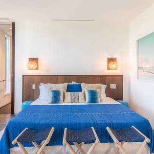Unwind in your serene bedroom where ocean blues meet crisp whites, warm lighting creates ambiance, and coastal artwork transports you to tranquil shores.