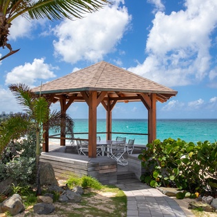 A serene beachside gazebo framed by swaying palms and lush greenery offers a private escape overlooking crystal-clear turquoise waters—perfect for morning coffee or sunset gatherings.