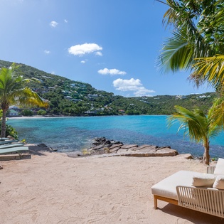 Stunning tropical beachfront with crystal-clear turquoise waters, palm trees, and hillside homes creating the perfect Caribbean paradise setting.