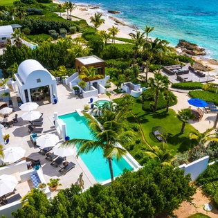 Beachfront villa complex with twin pools, lush tropical gardens, and pristine turquoise waters of the Caribbean coastline.