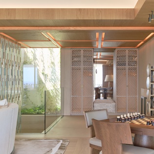 Unwind in your sophisticated living space with a chess table, warm wood accents, and garden views through floor-to-ceiling windows.