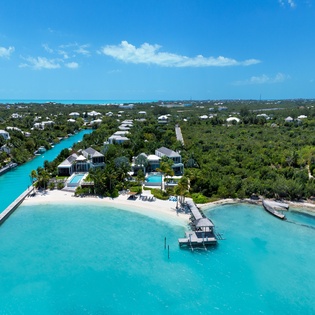 Aerial view of luxury waterfront villas surrounded by pristine turquoise waters and lush tropical landscape.