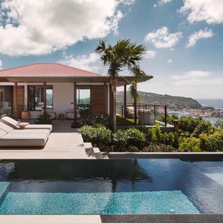 Modern villa overlooking turquoise Caribbean waters with infinity pool and tropical hillside setting.