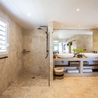 Relax in your private spa-like bathroom featuring travertine stone, a rainfall shower, and a thoughtfully designed double vanity with ample storage for your essentials.