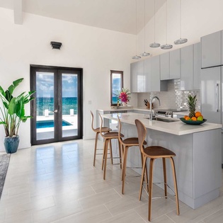 Step into a bright, modern kitchen with sleek cabinetry and waterfall island seating. The open design flows to your private terrace and sparkling pool, framing stunning ocean views.