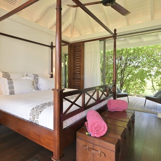 Your elegant four-poster bed invites restful sleep beneath vaulted ceilings, with garden views creating a peaceful tropical sanctuary.