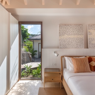 Wake up to tropical garden views from your bright bedroom, where natural light streams through floor-to-ceiling windows onto warm wood furnishings.